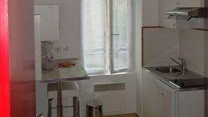 A compact kitchen with a window, a sink, a stove, and a trash can.