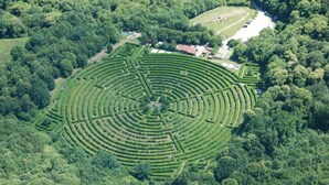 An aerial view of a large, circular maze-like garden with a central building and a parking area.