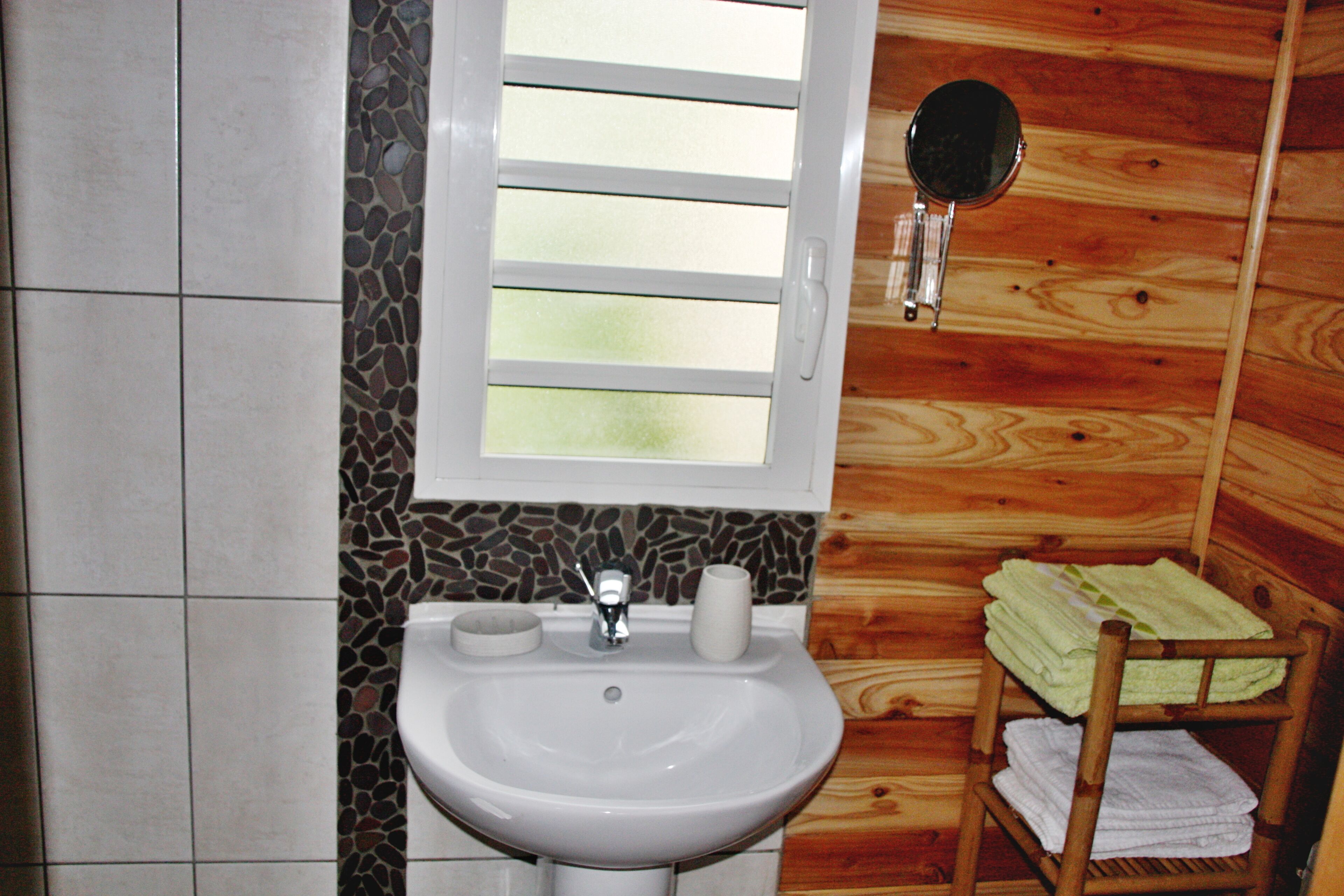 A bathroom with a white sink, a mirror, and a wooden chair with towels.