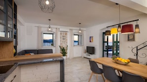 Una cocina moderna con encimera de madera, un comedor con mesa y sillas de madera, y un televisor sobre un mueble blanco.