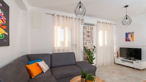Una sala de estar moderna con un sofá gris, una mesa de centro de madera y un televisor sobre un mueble blanco.
