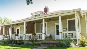 A two-story house with a covered porch, a chimney, and a front yard with grass and plants. - Front Porch, Sunny Coffee Nook, Gorgeous Bathroom, One block to CSU & Old Town! (Fort Collins)
