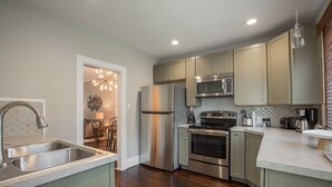 A modern kitchen with stainless steel appliances, a central island, and a dining area with a chandelier. - Front Porch, Sunny Coffee Nook, Gorgeous Bathroom, One block to CSU & Old Town! (Fort Collins)