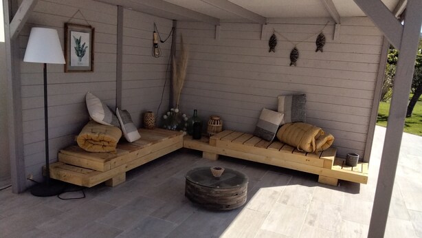 A cozy outdoor seating area with wooden benches and cushions, a lamp, and decorative wall hangings. - QUIET, COMFORTABLE PROVENCAL FARMHOUSE IN THE COUNTRYSIDE WITH SECURE SWIMMING POOL (Cheval-Blanc)