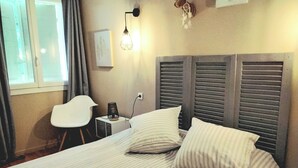 A neatly made bed with striped bedding, a bedside lamp, and a small table with a lamp. - QUIET, COMFORTABLE PROVENCAL FARMHOUSE IN THE COUNTRYSIDE WITH SECURE SWIMMING POOL (Cheval-Blanc)
