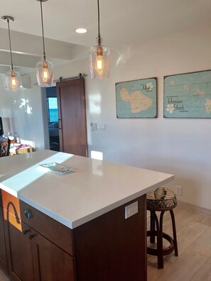 A kitchen with a central island, pendant lighting, wooden cabinets, and two wall-mounted maps of Hawaii. - Full Ocean View, Whale Watch from the Lanai
 Pool & Spa - 2B2B A/C. (Kihei)