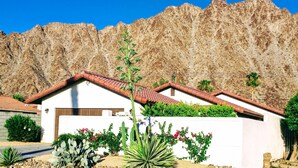 Ein Wohnhaus mit rotem Ziegeldach, umgeben von Wüstenpflanzen und einem felsigen Berg im Hintergrund.