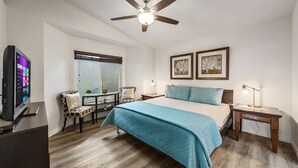 Ein Hotelzimmer mit einem Bett, einem Schreibtisch mit Computer, einem Sessel, einem Fenster und einem Deckenventilator.