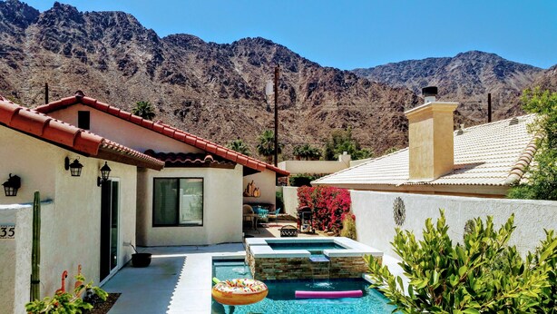 Ein Haus mit Swimmingpool, rotem Ziegeldach und einer Bergkulisse im Hintergrund.