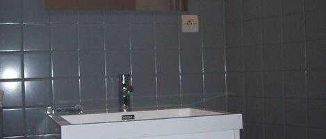 Ein Badezimmer mit einem weißen Waschbecken, einem Spiegel darüber und dunkel gefliesten Wänden.