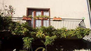 A two-story building with a balcony, a wooden bench, and potted plants.