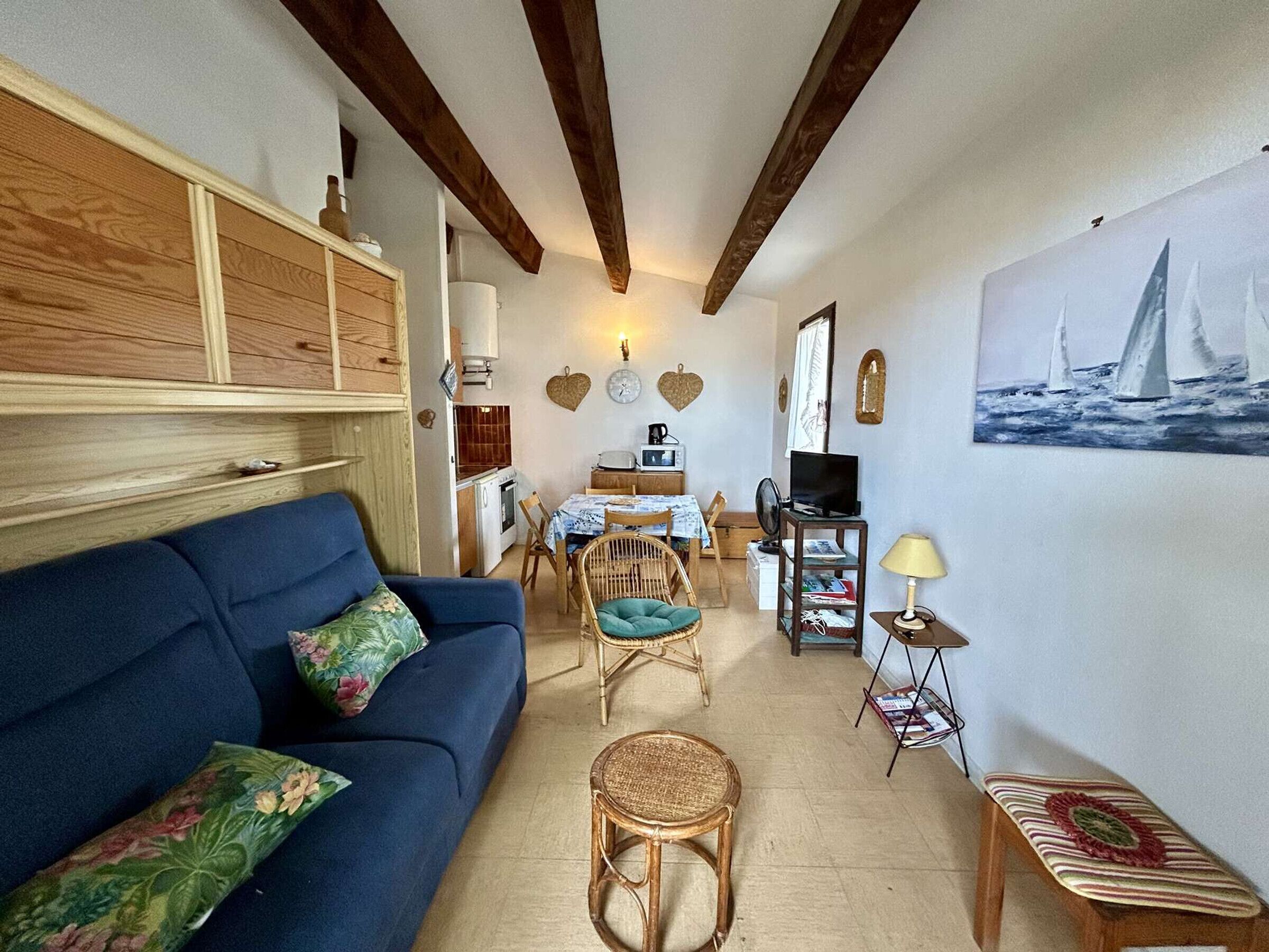 A cozy living area with a blue sofa, wicker chairs, a small table, and a painting of sailboats on the wall.