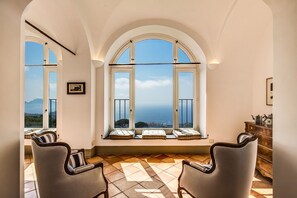 A room with arched windows overlooking a coastal view, a wooden cabinet, and two upholstered chairs. - Luxury historical wonderful 5 Master suites Villas with new pool, AC,Garden (MassaLubrense)
