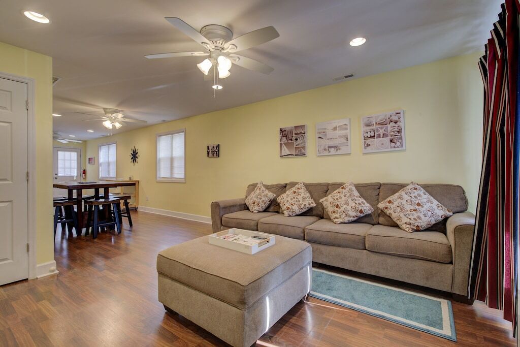 A living room with a sofa, ottoman, ceiling fan, and a dining area with a table and chairs.