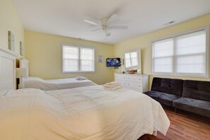 Un dormitorio con dos camas, ventilador de techo, televisor y sofá.