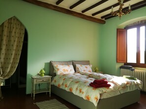 Un dormitorio con cama, mesita de noche, lámpara, radiador y ventana con cortinas.