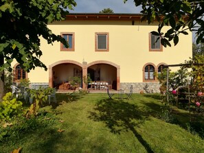 Un edificio de dos pisos con fachada amarilla, arcos y un patio cubierto con mesas al aire libre.