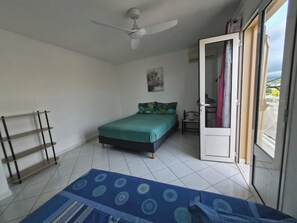 A bedroom with a bed, a ceiling fan, a door to a balcony, and a small table with a chair.