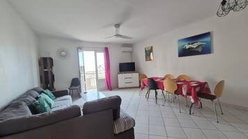 Un salon comprenant un canapé, une table à manger avec des chaises, un téléviseur et un ventilateur de plafond.