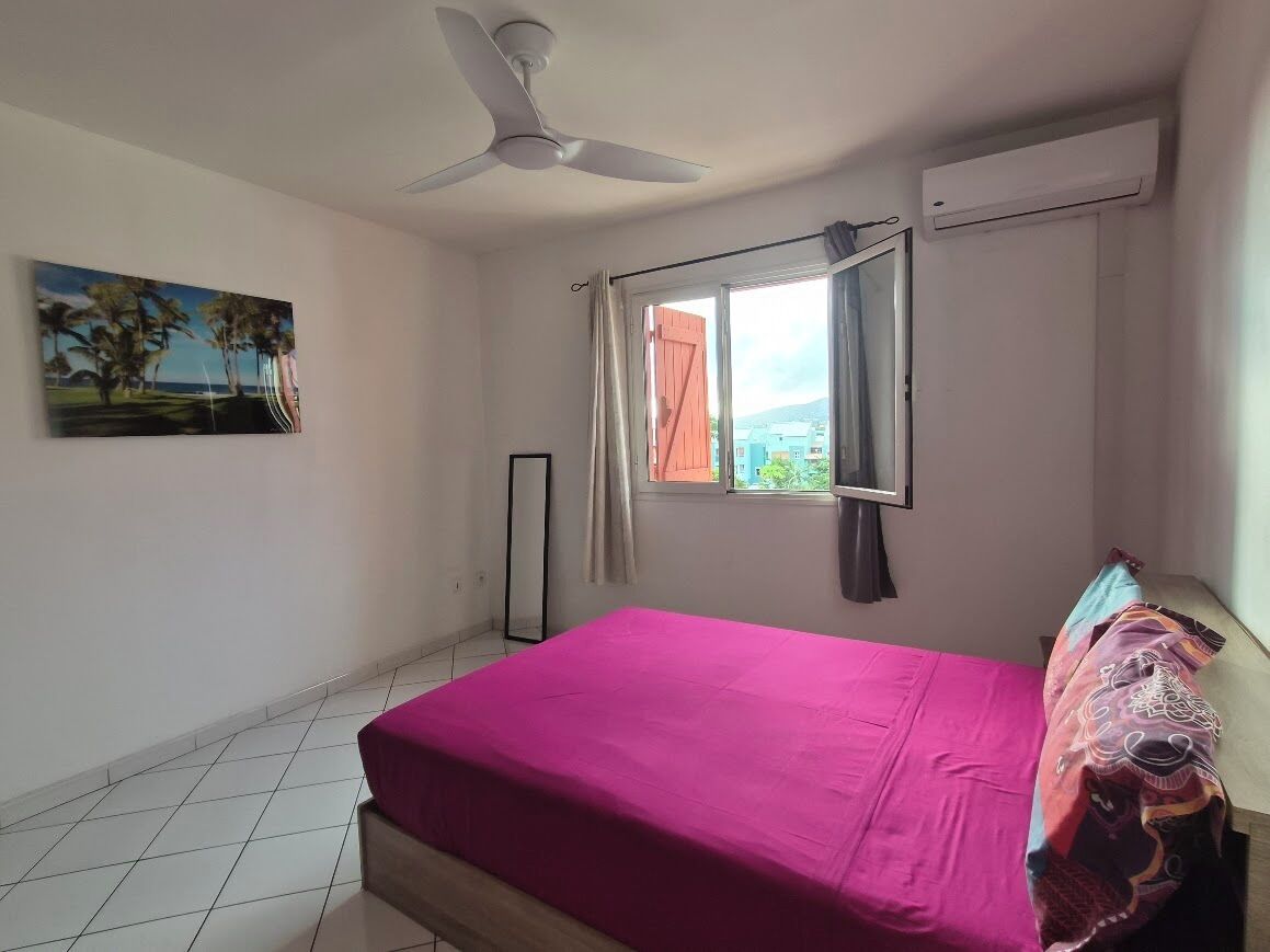 Une chambre à coucher avec un lit, un ventilateur de plafond, une fenêtre avec des rideaux et un tableau au mur.
