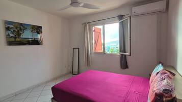 Une chambre à coucher avec un lit, un ventilateur de plafond, une fenêtre avec des rideaux et un tableau au mur.