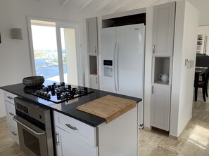 A modern kitchen with a gas stove, oven, white cabinets, and a refrigerator. - Carpe Diem, magnificent view of the marina (OYSTER POND)