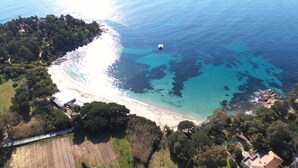 Vue aérienne d’une zone côtière avec une plage, des eaux d’un bleu limpide et une végétation luxuriante environnante.