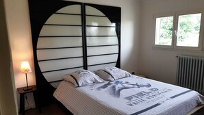 Un dormitorio con cama, mesita de noche, lámpara, ventana y radiador.