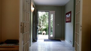 Un pasillo con piso de baldosas, una puerta que da al exterior y un pequeño jardín visible a través de la puerta.
