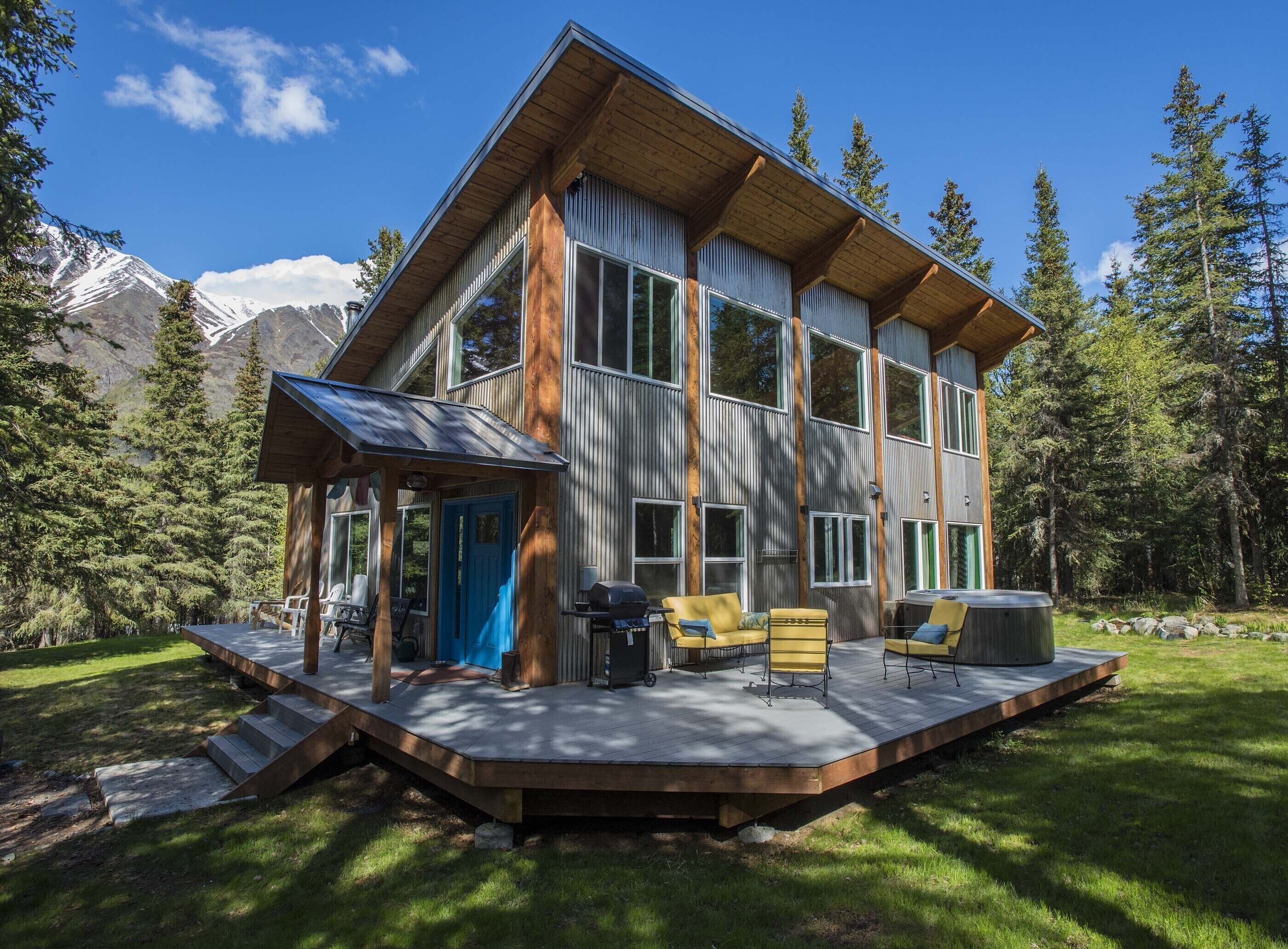 A modern two-story cabin with a deck, large windows, and a mountain backdrop.