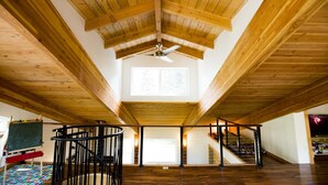 Um amplo loft com teto de madeira alto, um claraboia central, escada em espiral e uma grande janela.