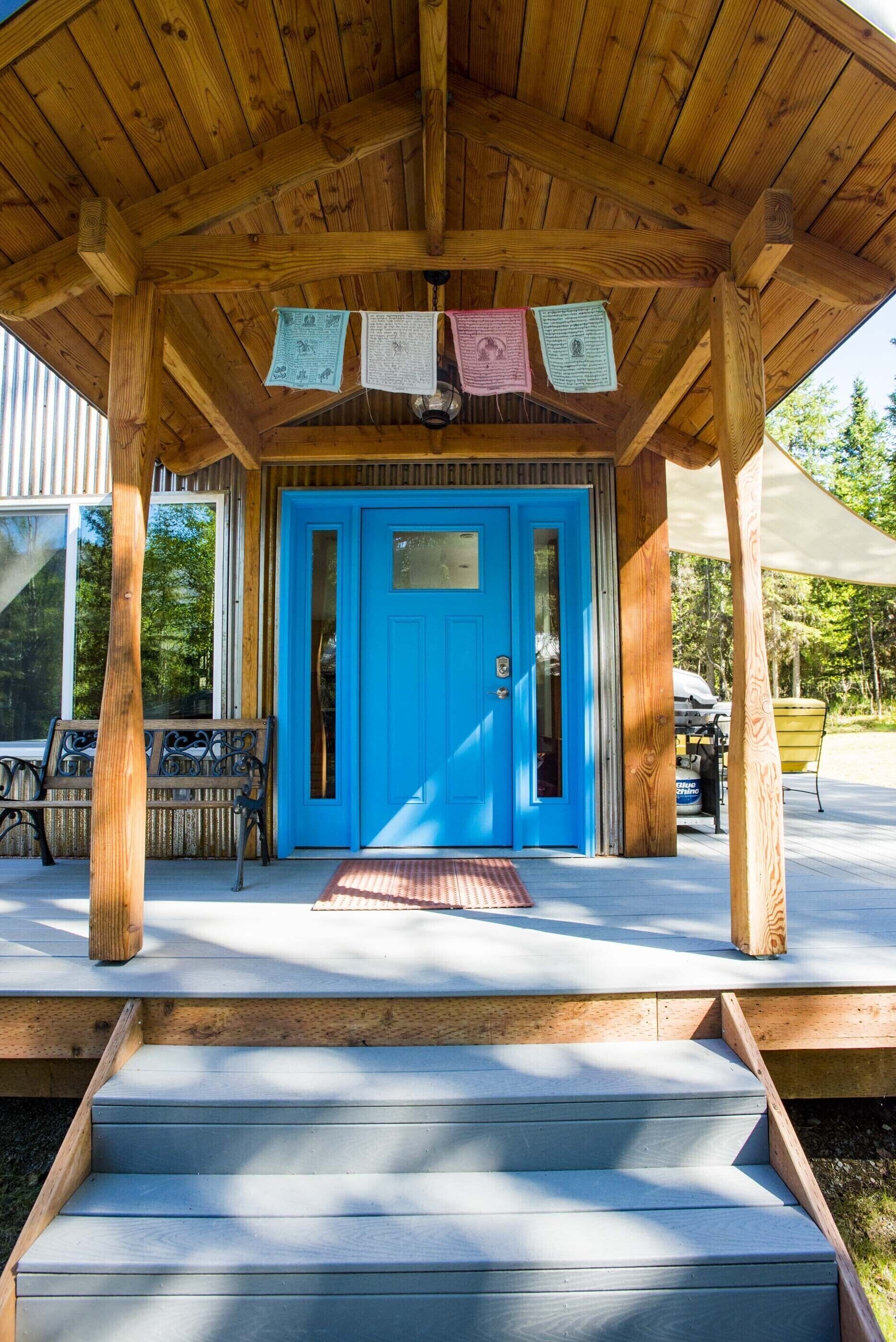 Une structure en bois avec une porte bleue et des marches menant à un porche abrité.
