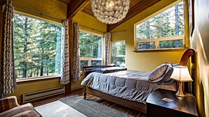 Quarto com uma cama grande, duas janelas, teto de madeira e um lustre.