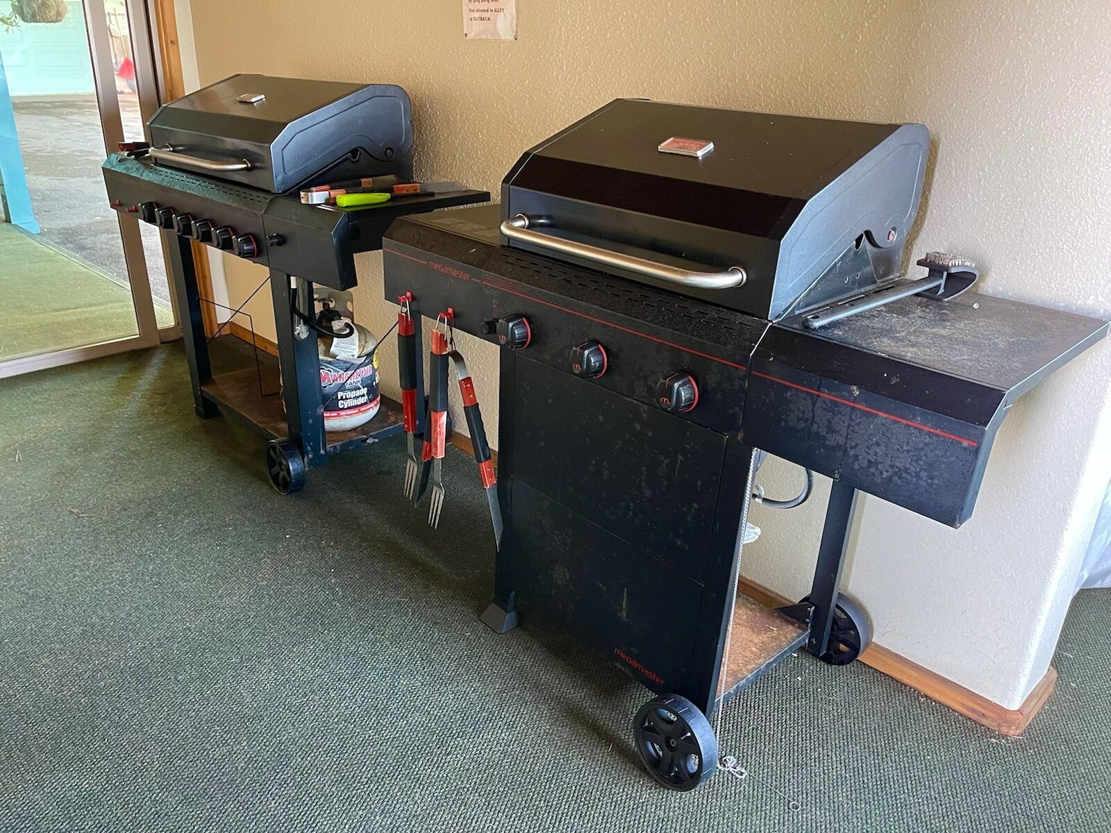 Een draagbare grillstation met wielen, een propaancilinder en een digitale thermometer.