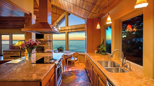 A kitchen with a large island, a stone fireplace, and a view of the ocean. - Inn Of The Lost Coast (Shelter Cove)
