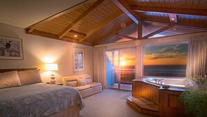 A bedroom with a large bed, a nightstand, a desk, and a window overlooking a sunset. - Inn Of The Lost Coast (Shelter Cove)