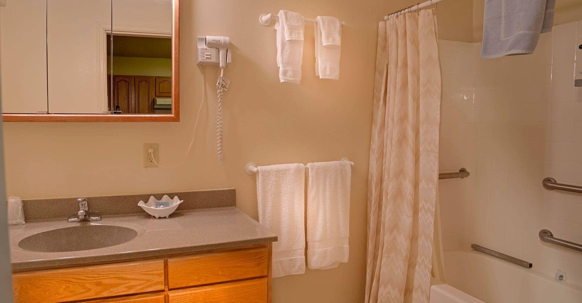 A bathroom with a sink, mirror, towel rack, shower curtain, and a hairdryer on the wall.