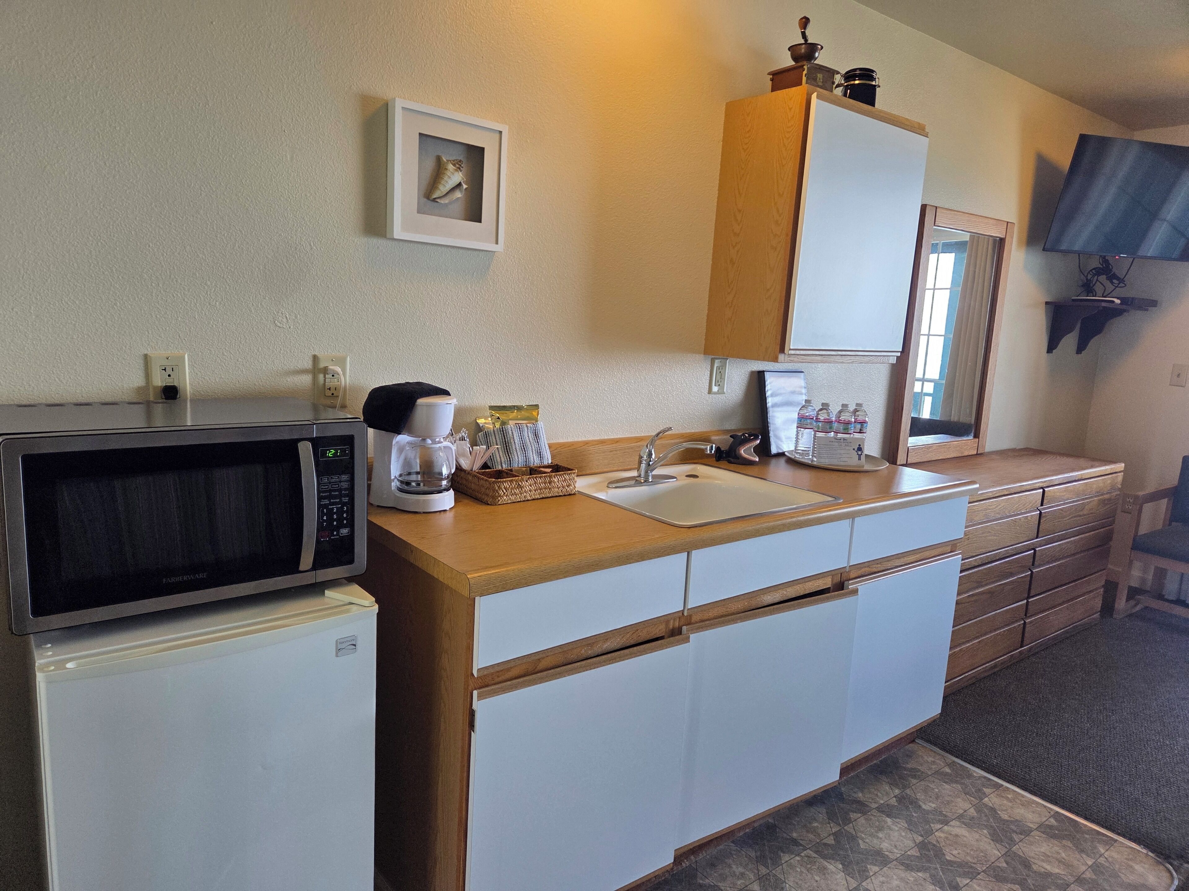 A compact kitchen with a microwave, coffee maker, sink, and wooden cabinets.