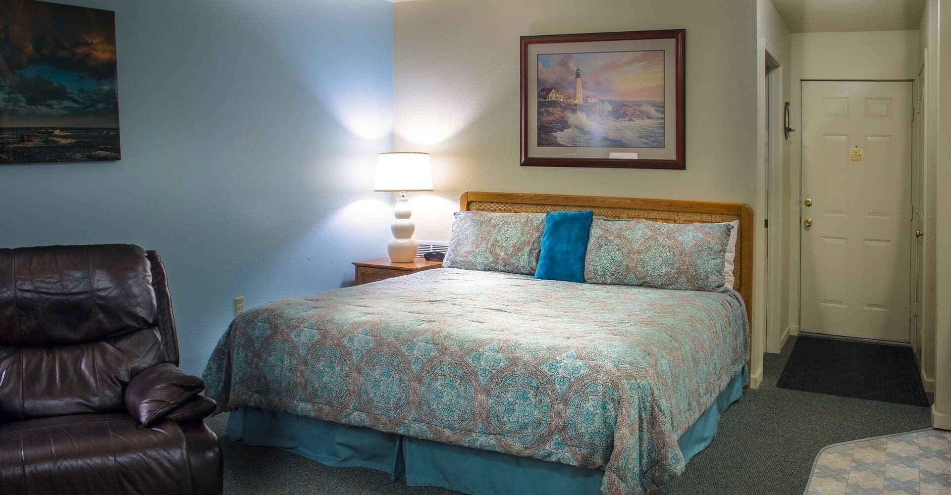 Una habitación de hotel con cama, una silla, una lámpara y un cuadro en la pared.