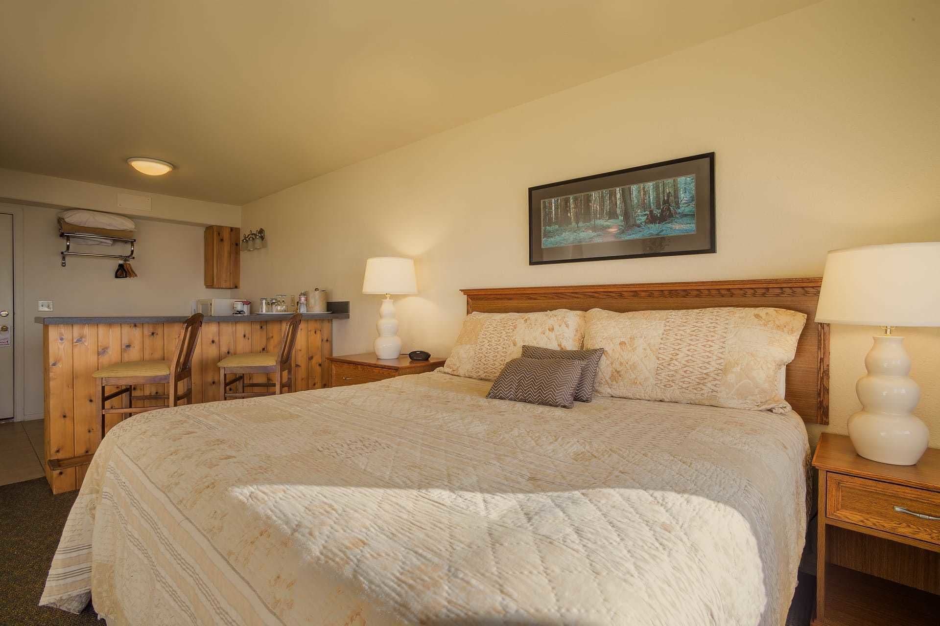 Un dormitorio con una cama grande, dos lámparas de noche, un cabecero de madera y un cuadro de un bosque en la pared.