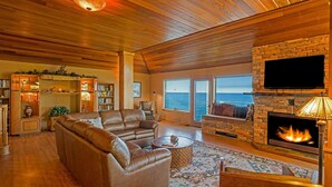 A cozy living room with a stone fireplace, leather sofas, and a large window overlooking the ocean. - Inn Of The Lost Coast (Shelter Cove)