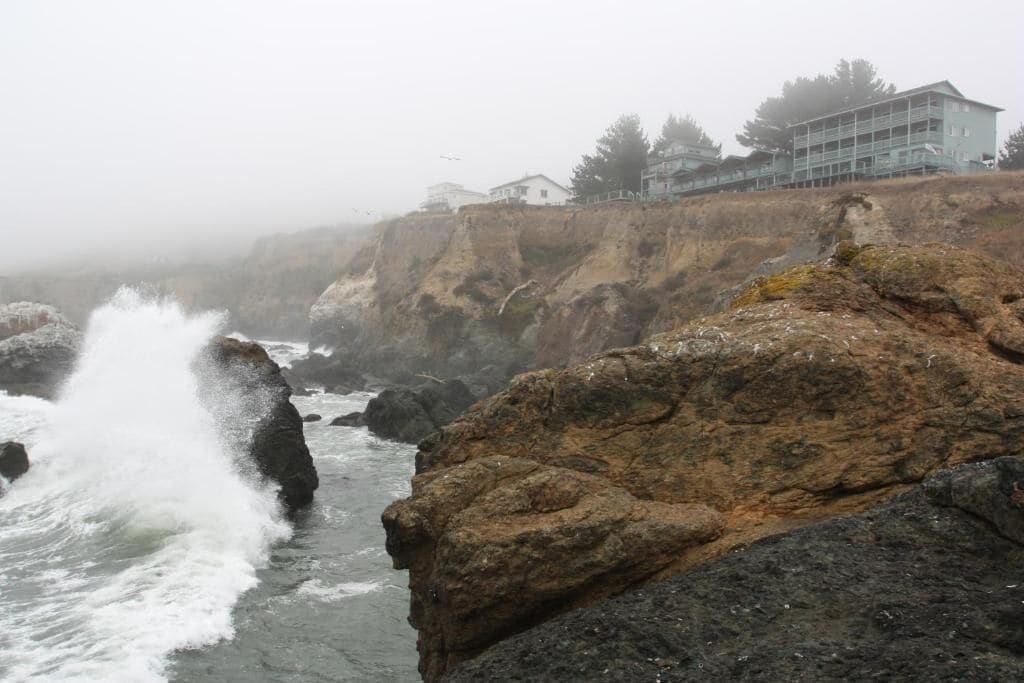 A coastal hotel with a rocky shoreline, waves crashing against the rocks, and a view of the ocean.