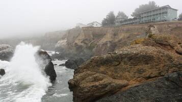 A coastal hotel with a rocky shoreline, waves crashing against the rocks, and a view of the ocean.