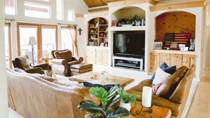 Un salon spacieux doté d’un grand téléviseur, de canapés en cuir, d’étagères en bois et d’une cheminée.