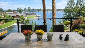 Un balcon donnant sur un lac, des fauteuils en osier, des seaux en métal remplis de fleurs et une petite statue d’ours.