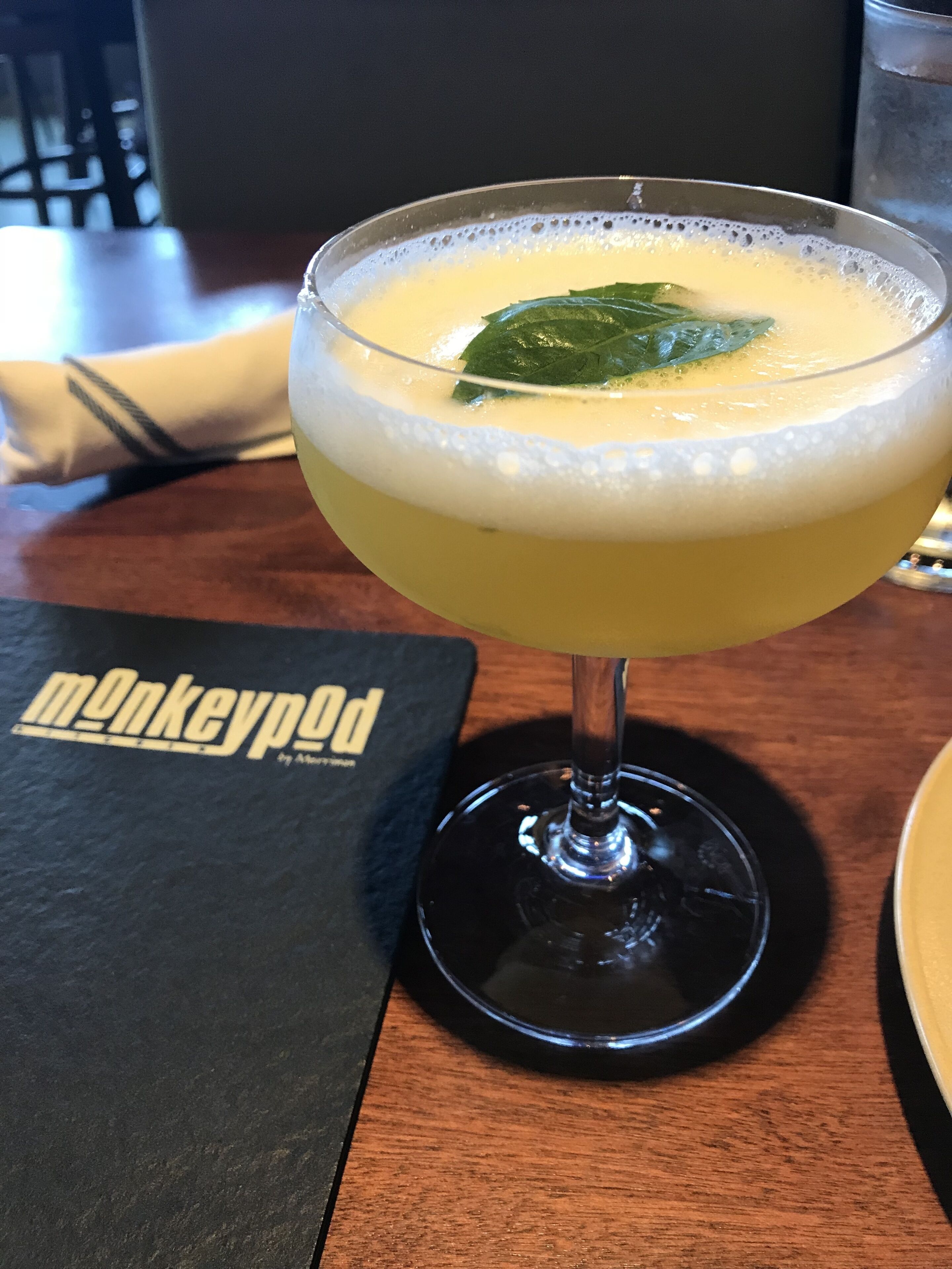 A cocktail in a stemmed glass with a foam head, placed on a coaster.