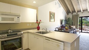 A modern kitchen with a microwave, stove, and dishwasher. There is a dining area with a table and chairs, and a view of the outdoors. - Quiet, Private Paradise M208 steps to the tropical pool and tennis court (Kihei)