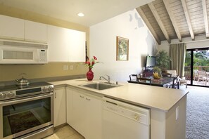 A modern kitchen with a microwave, stove, and dishwasher. There is a dining area with a table and chairs, and a view of the outdoors.
