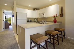 A compact kitchen with a central island, a refrigerator, a microwave, and a sink. There are three stools at the island.