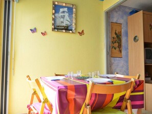Uma área de refeições com uma mesa posta para quatro pessoas, cadeiras com almofadas coloridas, um quadro na parede e uma porta com painel decorativo.